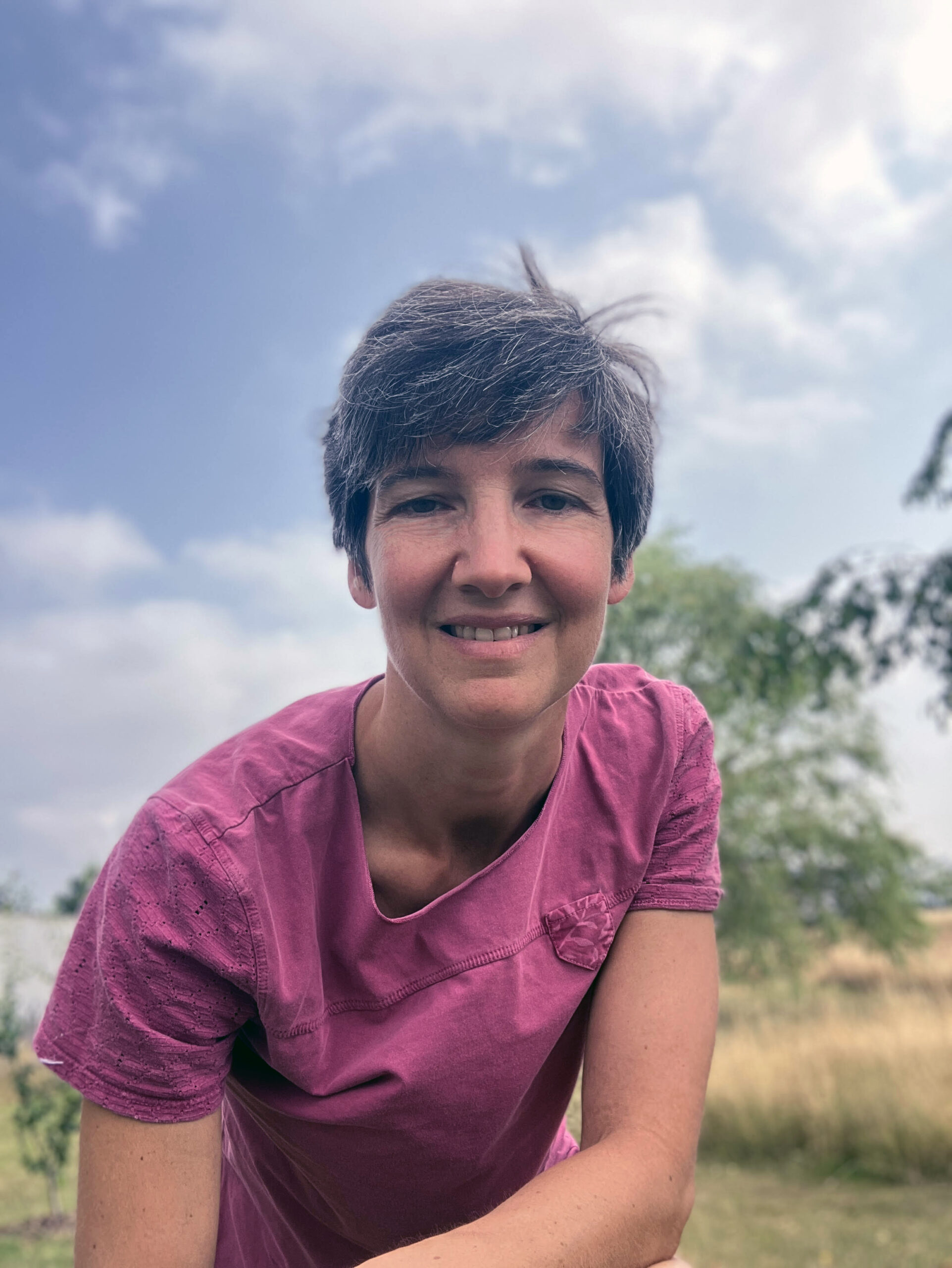 portrait de Marie Laffont souriante en extérieur, avec une blouse de praticienne bordeaux